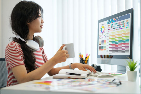 Side view of young woman sitting at graphic studio and choosing color for creative project on computer screen.