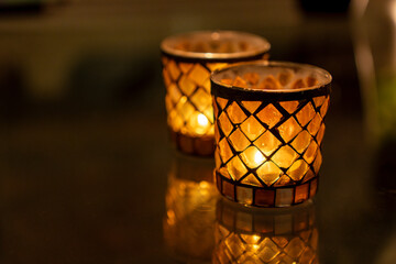 two small glass candlesticks with a diamond pattern with flickering flames against a dark background with space for text