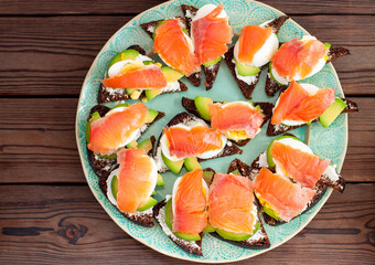 Set of bruschettas with rye bread, salmon and cream cheese on a dark wooden natural background