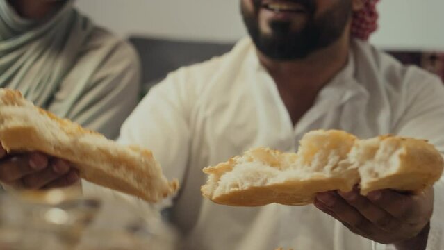 Cropped closeup of unrecognizable bearded islamic man breaking pita bread and sharing it with closest family members during festive meal on end of Ramadan month celebrating Eid al-Fitr