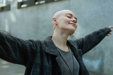 A happy young woman with a shaved head is smiling and dancing in the street.
