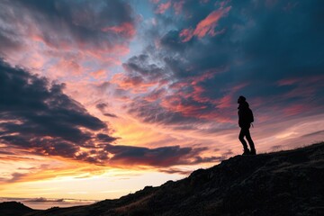 the silhouette of a person standing on a hill, surrounded by a breathtaking sunset, with the colorful sky and clouds dominating the frame