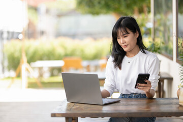 Young Asian woman using smartphone and laptop in outdoor cafe, self-employed