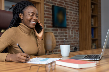 Smiling woman with dreadlocks working with laptop and smartphone is freelance entrepreneur