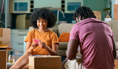 Young Couple Playing Cards In New Home On Moving Day Drinking Wine