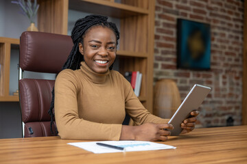 Joyful woman with dreadlocks using tablet engaged in distance work holding device