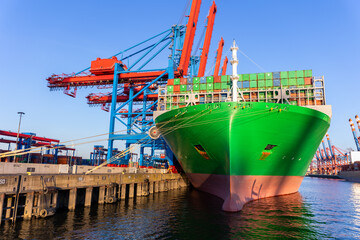 Scenic view giant cargo container ship loading Hamburg city port harbor against seaport cranes warm...