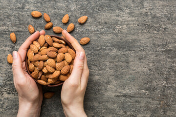 Woman hands holding a wooden bowl with almond nuts. Healthy food and snack. Vegetarian snacks of different nuts - obrazy, fototapety, plakaty