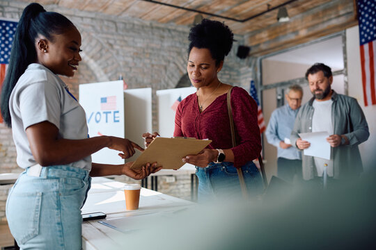 Polling place volunteer assisting black woman to sign up for voting during USA elections.