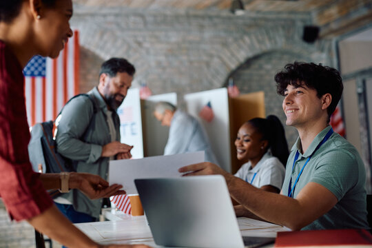 Happy volunteer giving ballot to a voter at polling place during US elections.