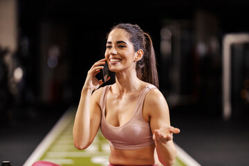 Portrait of a sportswoman talking on a cellphone in a gym. - obrazy, fototapety, plakaty