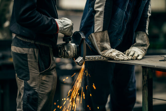 Cropped picture of two metallurgy workers grinding and cutting metal parts at heavy industry plant.