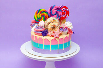 Cololrful and bright birthday cake with lollipops and sweets over a purple background with copy space