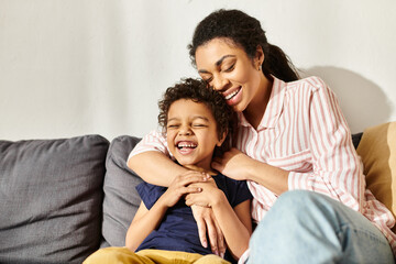 Fototapeta premium cheerful loving african american mother hugging her adorable smiling son while in living room