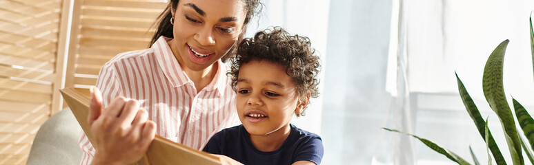 merry appealing african american woman in cozy attire reading book to her little son at home, banner