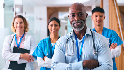 Portrait Of Smiling Multi Cultural Medical Team Wearing Scrubs And White Coats In Modern Hospital 