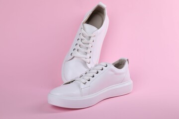 Pair of stylish white sneakers on pink background