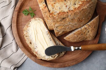 Tasty bread with butter and knife on grey textured table, top view