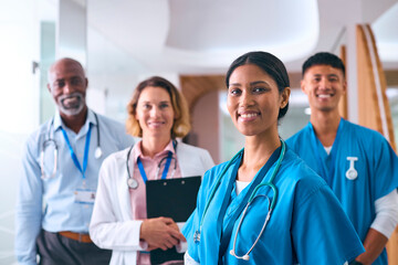 Portrait Of Smiling Multi Cultural Medical Team Wearing Scrubs And White Coats In Modern Hospital 