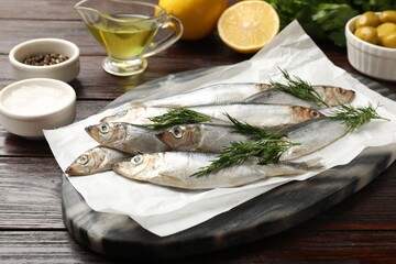 Fresh raw sprats, dill and other products on wooden table, closeup