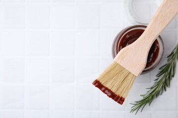 Marinade in jar, rosemary and basting brush on white tiled table, flat lay. Space for text