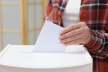 Woman putting her vote into ballot box on blurred background, closeup