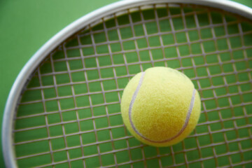 yellow tennis ball lies on a tennis racket on a green background