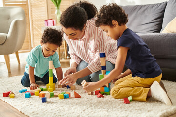 joyful attractive african american mother in cozy outfit playing with toys with her little cute sons