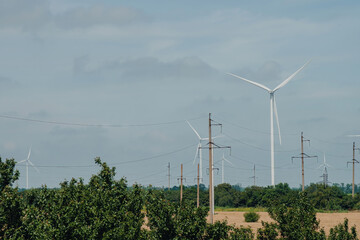 Windmills generate alternative form of energy on farm field against forest. Wind turbines produce...