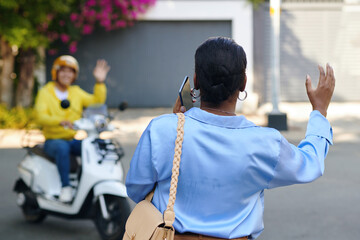 Woman waving motorbike taxi driver to attract his attention, view from back
