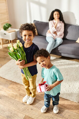 focus on merry african american kids with tulips and gift posing near their blurred mom, Mothers day