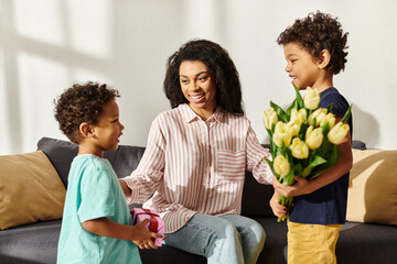 Obraz na płótnie Canvas joyful african american woman receiving gift and tulips from her loving little sons, Mothers day