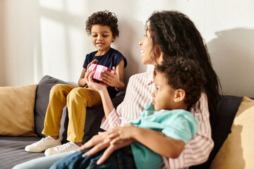 focus on little jolly african american boy holding present next to his mom and brother, Mothers day