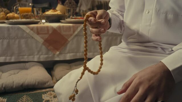 Side tilt footage of young Arab muslim man in traditional apparel using tasbih while performing namaz at home on Eid al-Fitr day