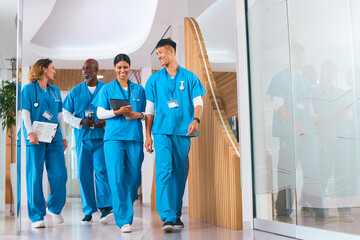 Multi Cultural Medical Team Wearing Scrubs Walking Along Corridor In Modern Hospital 