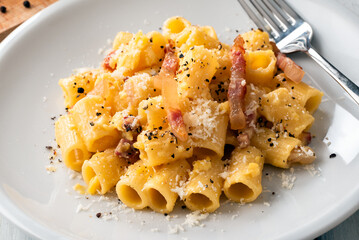 Deliziosi rigatoni alla carbonara, ricetta tipica della cucina romana di pasta con uova, guanciale, pecorino e pepe nero, cibo italiano 