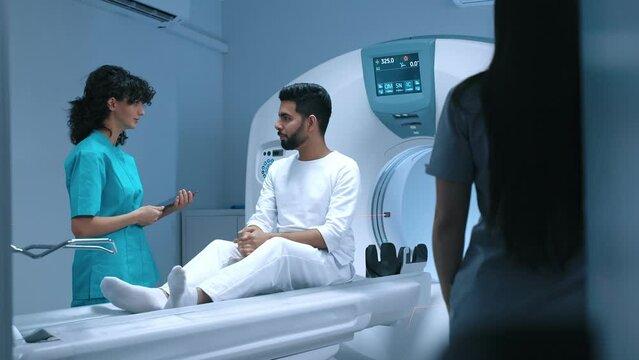 Professional radiologist using tablet, consulting patient before undergoing diagnostics using MRI machine in medical center. Patient getting recommendations from doctor before x-ray procedure.