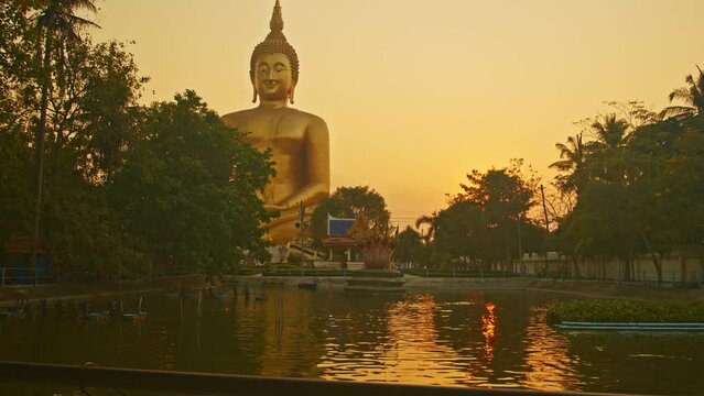 scenery yellow sky at sunset behind the biggest buddha..reflection of yellow sky in the pool. .golden big buddha popular landmark at wat Muang Ang Thong Thailand..