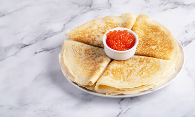 Pancakes with red caviar on a marble table
