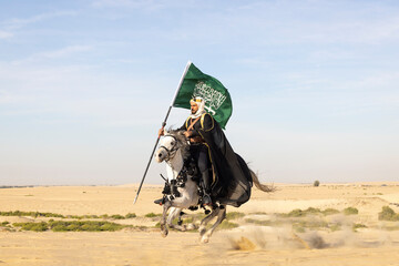 Saudi man in traditional clothing in the desert with a white horse, carrying a flag of Saudi Arabia