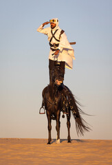 Saudi man in a desert standing at the back of his  black stallion