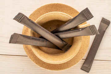 Several paper sticks with sugar in a ceramic cup on a wooden table, macro, top view.