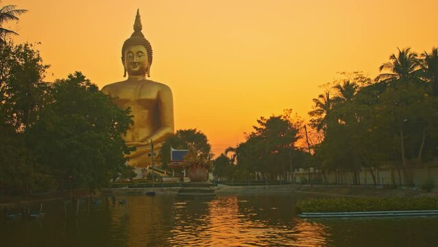 scenery yellow sky at sunset behind the biggest buddha..reflection of yellow sky in the pool. .golden big buddha popular landmark at wat Muang Ang Thong Thailand..