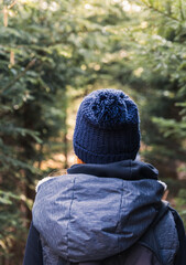 Young woman from back with redheaded in knitted hat walking in forest