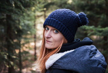 Portrait of young redheaded woman in knitted hat with coniferous forest in background