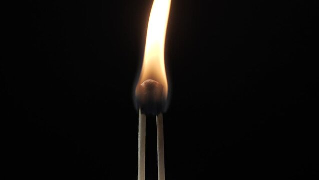 Two matches stuck together burning against a black background. 