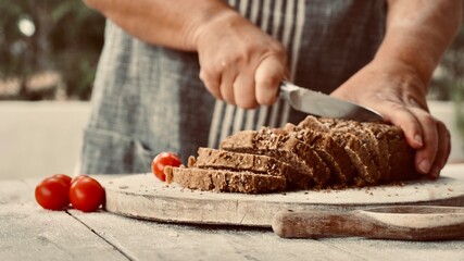 Woman in apron with close-up hands cutting homemade whole wheat bread.