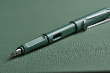 Green fountain pen lies green leather tabletop desk.