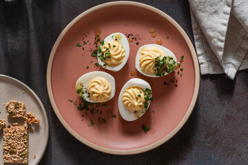 Deviled eggs with spicy oil and herbs, flatbread crackers, Easter party appetizer, directly above - 750797167