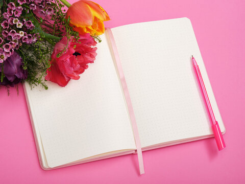 Colorful tulips lie on empty page of notebook, pink background. Space for your text.
